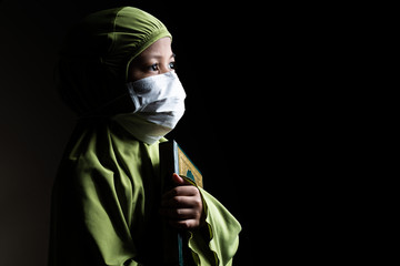 Muslim girl with her Quran. Wearing a surgical mask. Covid-19 and coronavirus concept.