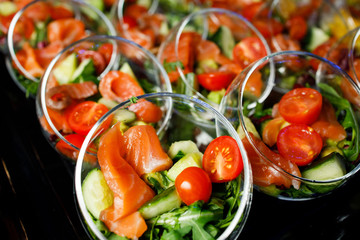 Top of buffet table with glass cups with salad of red fish, tomatoes, cucumber