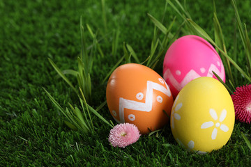 Fototapeta na wymiar Colorful Easter eggs and daisy flowers in green grass, closeup