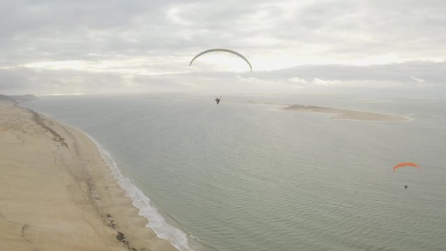Aerial view of paragliders flying above the beach and sand dunes. Coastal landscape, outdoor sport, and freedom concept.