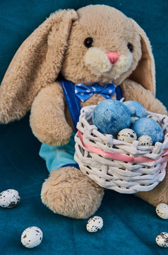 easter toy bunny holds easter basket with blue painted eggs and little queil eggs