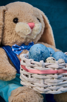 easter toy bunny holds easter basket with blue painted eggs and little queil eggs