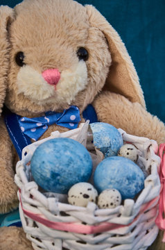 easter toy bunny holds easter basket with blue painted eggs and little queil eggs