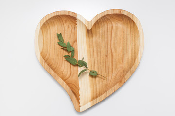 handmade wooden heart-shaped plate with green twig on the table