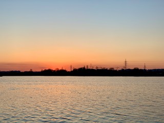 Obraz premium At sunset, a beautiful sky is displayed in the river. On the horizon, the shore is forcing. The sun sets over the horizon of the reservoir.