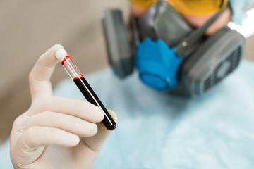 A doctor in protective clothing is carefully looking at a blood sample in a test tube.