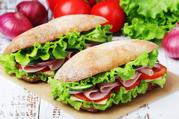 Two sandwiches with fresh vegetables, ham and cheese in ciabatta bread	