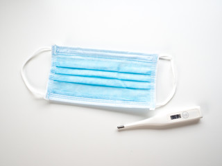 Blue surgical mask and digital thermometer on white background.