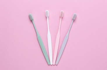 Pink, green, white and gray toothbrushes on pink background. Taking care of teeth, dental concept. Flat lay photo, copy space, top view.