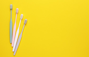 Pink, green, white and gray toothbrushes on yellow background. Taking care of teeth, dental concept. Flat lay photo, copy space, top view.