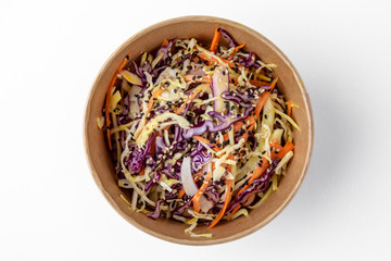 Fresh cabbage and carrot salad in a paper bowl for take away or food delivery isolated on a white background.