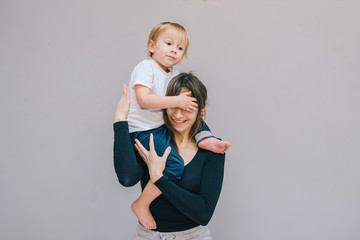 mom plays with a naughty son against a gray wall