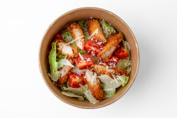 Salad of fresh herbs, lettuce, chicken fillet in a batter in a paper bowl for take away or food delivery isolated on a white background.