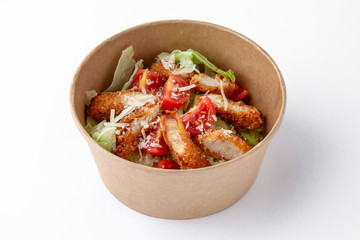 Salad of fresh herbs, lettuce, chicken fillet in a batter in a paper bowl for take away or food delivery isolated on a white background.