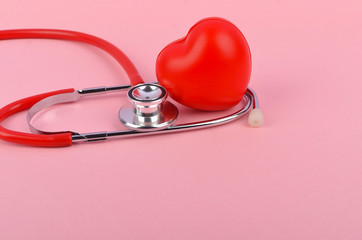 Red heart with stethoscope on pink background. Heart health care concept. Selective focus.
