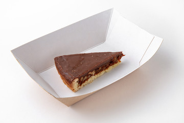 Dessert slice of chocolate cake in a paper plate for take away or food delivery isolated on a white background.