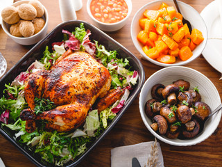 Decorated festive table with whole roasted chicken, salad, pumpkin, mushrooms, beans and walnut. The concept of family dinner or Thanksgiving celebrate.