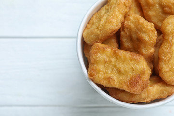 Bucket with tasty chicken nuggets on white wooden table, top view. Space for text