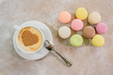 Multi-colored macarons with cappuccino on a table in a coffee shop. Sweet and tasty food