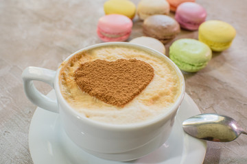 Multi-colored macarons with cappuccino on a table in a coffee shop. Sweet and tasty food