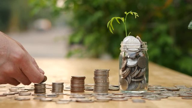 Saving money hand putting coins on stack on table with sunshine on nature background.