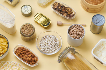 Creative flatlay with pantry staples. Glass jars with pasta, beans and chickpeas, canned goods,...