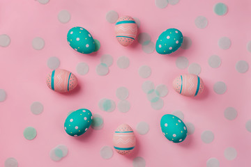 Pink and mint colored decorated eggs on pink background with confetti. Easter concept, natural frame with copy space