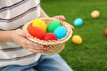Fototapeta na wymiar Cute little boy with basket full of Easter eggs outdoors, closeup