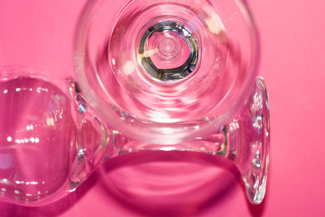 Glass transparent wine glasses on leg on pink background. Highlights and shadows on the dishes.