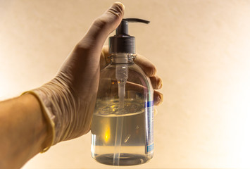 Hand with disposable glove holding glass of alcohol gel against covid-19