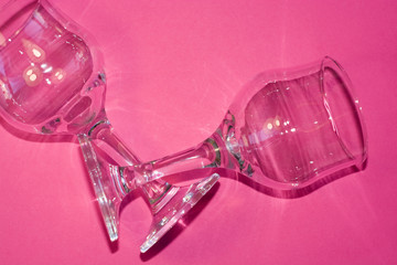 Glass transparent wine glasses on leg on pink background. Highlights and shadows on the dishes.