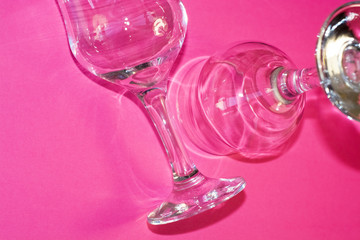 Glass transparent wine glasses on leg on pink background. Highlights and shadows on the dishes.