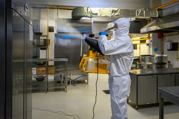 man in protective equipment disinfects with a spray gun industrial surfaces due to coronavirus...