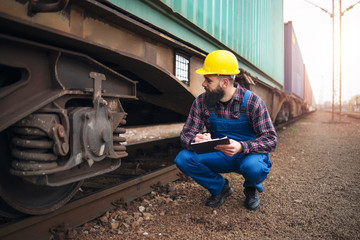 Fototapeta na wymiar Railroad worker checking up wheels and braking system of freight train. Safety inspector or maintenance engineer checking rail tracks at station.