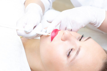 Young woman having permanent makeup on her lips at the beauticians salon. Permanent Makeup (Tattoo). drawing a contour with a white lip pencil