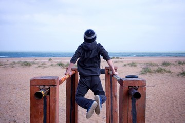 Young boy push ups on the parallel dips on a beach and look on the ocean. Motivation sport.
