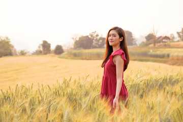 Asian young woman walking and relaxing in barley field at sunset, holiday lifestyle activities, happy traveler in modern agriculture field 