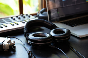 Headphones in a music producer home studio, desk with digital recorder, notebook and Midi. Window with nature in the background.