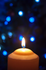 A large candle burns against the background of a garland with shining lights. Vertical photo, defocus. Mystic esoteric romance divination mood christening Christmas carol setcers.