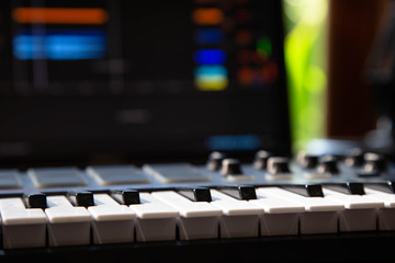 Close up of a Midi keyboard in a music producer home studio. Laptop screen in the background.