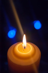 A large candle burns against the background of a garland with shining lights. Vertical photo, defocus. Mystic esoteric romance divination mood christening Christmas carol setcers.