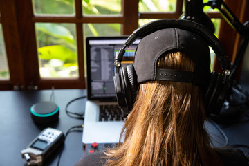 Close up of a female music producer with headphones in her home studio, desk with digital recorder,...