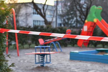 Red caution tape on kids playground, closed due to COVID-19 quarantine. Selective focus.