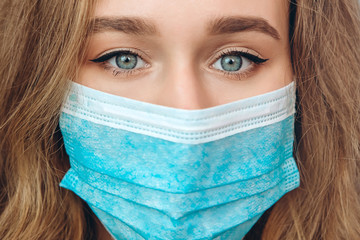 a close-up portrait of a girl in a medical mask on a blue background. A frightened woman. The girl is afraid of contracting coronavirus. COVID-2019. A global pandemic.
