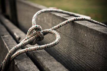 Old and worn-out rope knotted, resting on a wooden bench outdoor