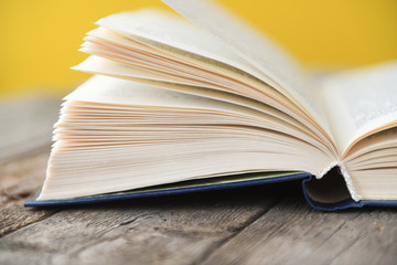 An open book on an old wooden table on a yellow background.