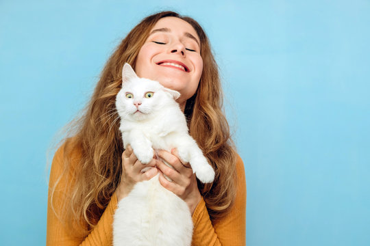 A young girl is holding a white cat in her arms. Portrait of a curly-haired blonde girl on a blue background. The concept of animal protection. Take the cat from the shelter.