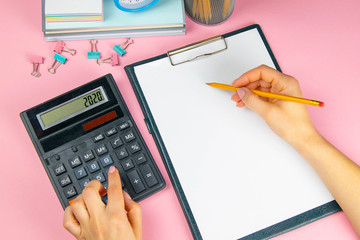 The hands of a woman count on a calculator and write notes. Top view of business woman's hands on white sheet. Finance and business concept