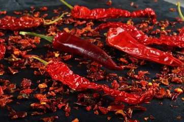 chili flakes and dried chili peppers on a black stone background