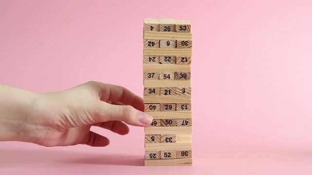 Woman and man plays jenga on pink background. Family recreation and holidays concept.